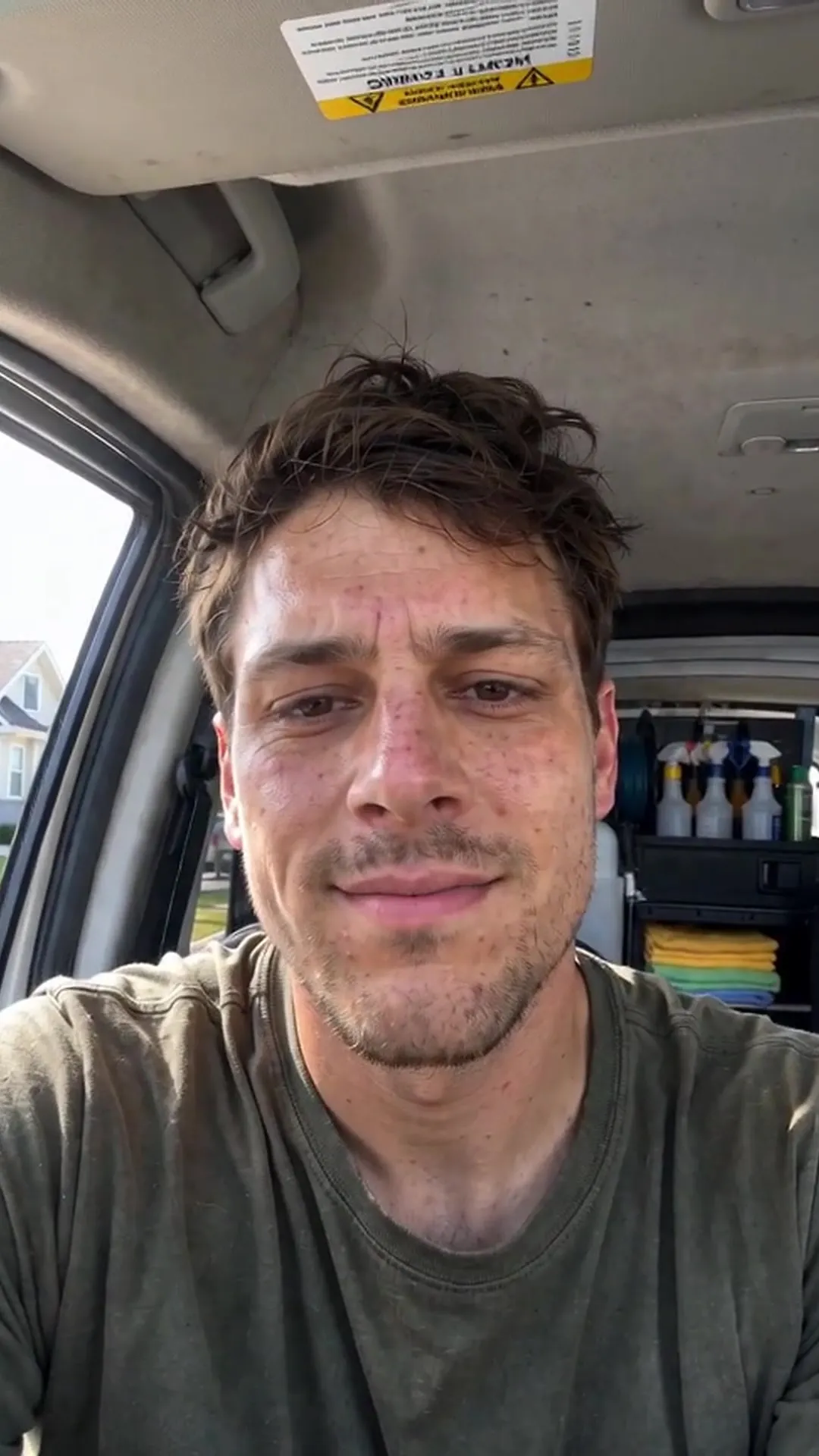 A detailer sitting in the cab of his van, shelves of bottles and folded towels behind him.